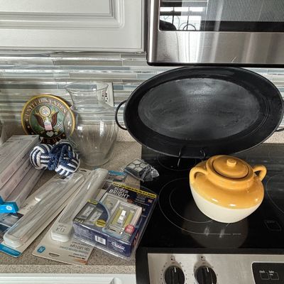 An assortment of household goods including an oval black roaster pan, a yellow and white stoneware bean pot, a clear glass vase, packaged...