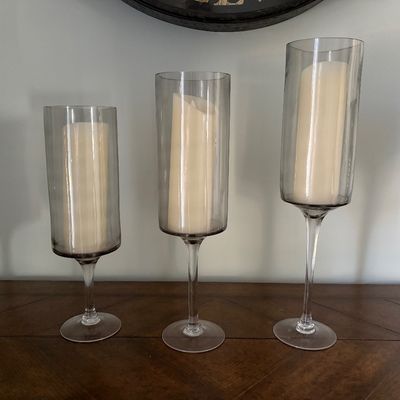 Set of three graduated smoked glass hurricane candle holders on stems with cream pillar candles.