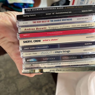 Stack of 10 compact discs featuring rock, pop, and classical artists including Santana, The Allman Brothers Band, and Sheryl Crow.