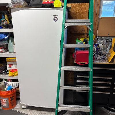 Green fiberglass stepladder standing in front of a white Whirlpool upright freezer