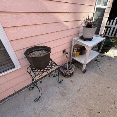 Outdoor patio assortment featuring a white metal two-tier rolling cart, a green wrought iron plant stand with an octagonal planter, a...