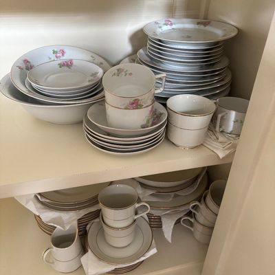 Vintage fine china dinnerware service featuring floral rose motifs and gold rim accents, neatly stacked in a cupboard.