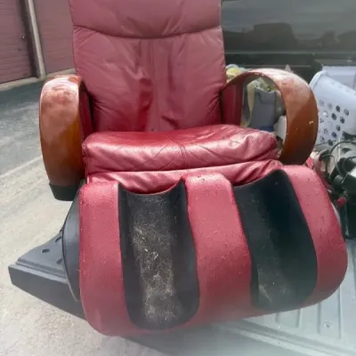 Red faux-leather electric massage chair with wooden armrests, showing heavy wear and scuffing on the leg rest.