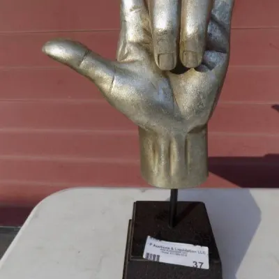 Silver-toned sculpture depicting the 'I love you' sign language hand gesture, mounted on a dark stepped base.