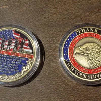 Pair of military appreciation challenge coins in protective clear plastic cases, featuring American flag motifs, a bald eagle profile,...