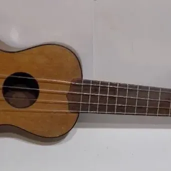 Vintage soprano ukulele with a natural wood finish, dark fretboard, and metal tuning pegs, showing light wear.