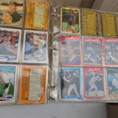 Open binder of late 1980s Major League Baseball trading cards housed in clear plastic sleeve pages, featuring players like Ryne Sandberg...