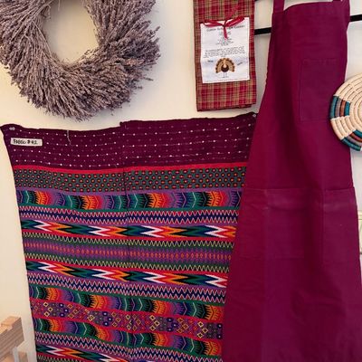 Collection of kitchen items and textiles including a purple apron, dried lavender wreath, woven colorful fabric wall hanging, and woven...