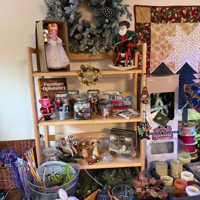 Wooden display shelf holding a variety of holiday decorations, craft supplies, figurines, and vintage collectibles.