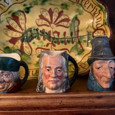 Trio of vintage ceramic character jugs depicting historical figures, displayed in front of a hand-painted floral serving platter.