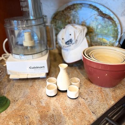 Vintage Cuisinart DLC-X Plus food processor displayed alongside a set of ceramic mixing bowls and a sake bottle with cups on a kitchen...