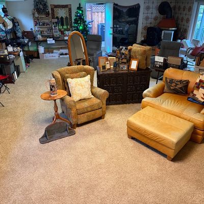 Spacious estate sale showroom featuring a golden-yellow leather oversized armchair with matching ottoman, a patterned upholstery wingback...