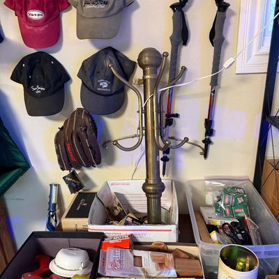A brass coat rack surrounded by baseball caps, trekking poles, a baseball glove, and various household items organized in boxes.