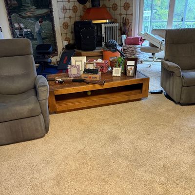 Pair of contemporary grey microfiber power recliners flanking a long wooden coffee table displaying picture frames and collectibles.