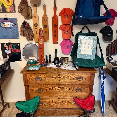 Vintage oak dresser with leaf-carved drawers, displayed alongside baseball mitts, wooden paddles, caps, and stadium seats hanging on the...