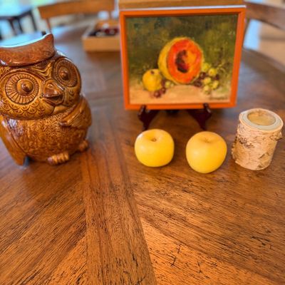 Vintage ceramic owl cookie jar alongside a small framed still life oil painting of fruit, two artificial yellow apples, and a birch bark...