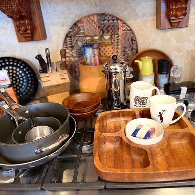 Collection of kitchen items including a wooden divided tray, non-stick cookware, coffee press, mugs, and wooden bowls.