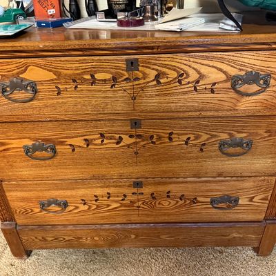 Antique oak three-drawer dresser featuring inlaid vine details, keyholes, and ornate metal bale handles.