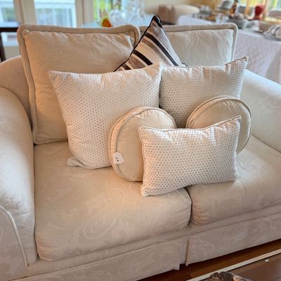 Cream-colored jacquard upholstered loveseat arranged with an assortment of studded and round accent pillows.