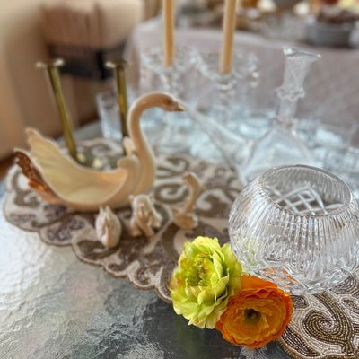 Tabletop display featuring a ceramic swan planter, small animal figurines, a cut crystal rose bowl, and clear glass candlesticks on a...