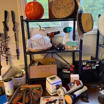 Black metal shelving unit displaying a collection of household items, including a glowing jack-o'-lantern, woven baskets, hand...