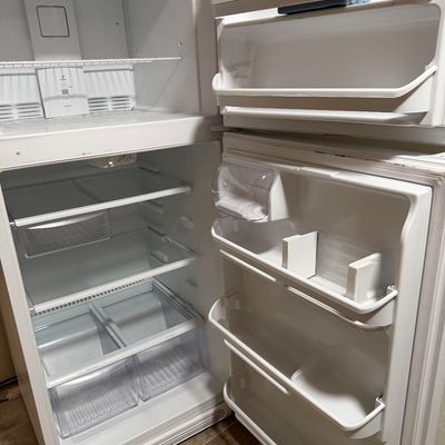 White top-freezer refrigerator shown open, featuring adjustable glass shelves, door bins, and lower crisper drawers.