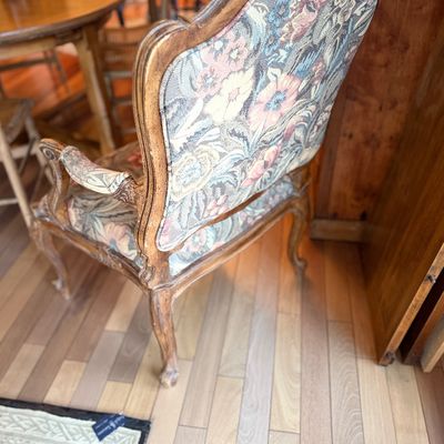 French Provincial style armchair featuring a carved wooden frame with a distressed finish and floral tapestry upholstery.