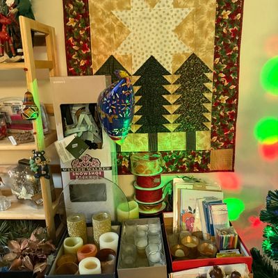 Holiday decor display featuring a quilted Christmas tree wall hanging, boxed Winter Walker snowshoes, rolls of ribbon, and various candle...