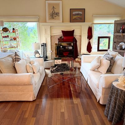 Living room setup featuring a pair of off-white upholstered sofas, a glass-topped chrome coffee table, and various home decor pieces near...