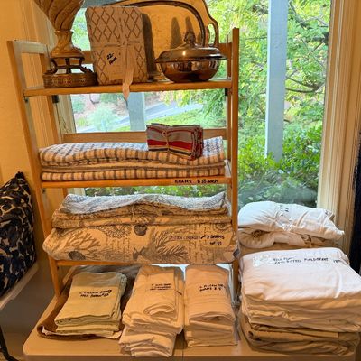 household linens, including bed sheets, pillow shams, and coastal-patterned coverlets alongside silver-plated serving pieces.