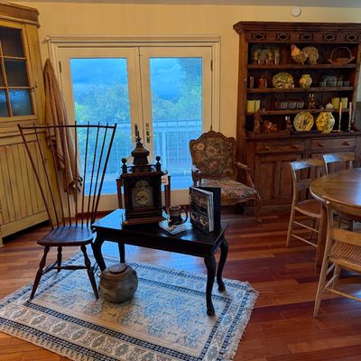 Rustic dining room setup featuring a large dark wood hutch filled with decor, a yellow painted corner cabinet, an ornate mantle clock on...