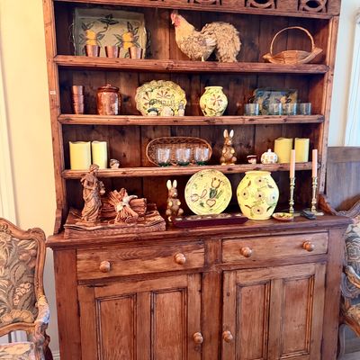 Rustic pine hutch featuring carved geometric upper detailing, open shelves, two drawers, and a lower double-door cabinet, filled with...
