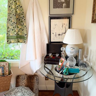 A room corner displaying a glass-top accent table with crystal decanters and small accessories, framed artwork on the wall, hanging...