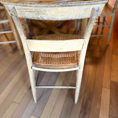 Vintage painted wooden dining chair with a woven cane seat, featuring a distressed finish and curved backrest.