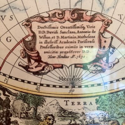 Detailed view of an ornate, vintage-style world map featuring a Latin cartouche dated 1630 and illustrations of animals along the bottom.