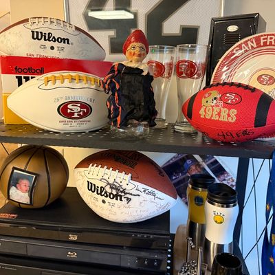 Collection of sports memorabilia featuring San Francisco 49ers footballs, glassware, and decorative plates, alongside electronics...