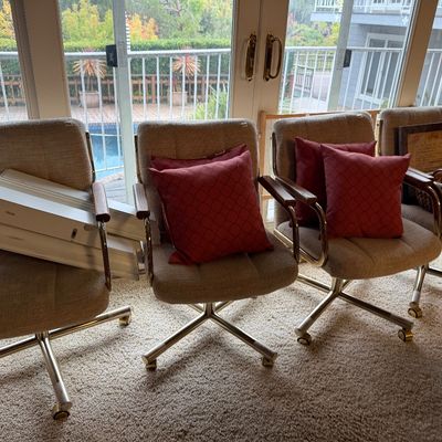 Set of four mid-century modern rolling armchairs featuring beige textured upholstery, wooden armrests, and chrome bases.
