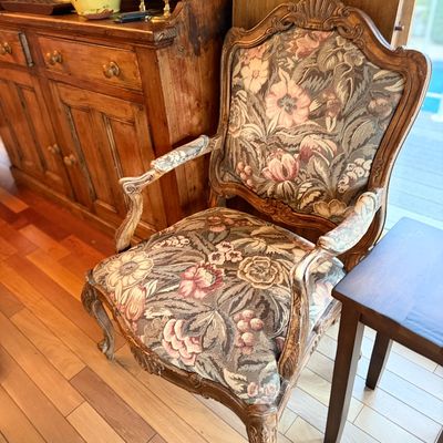 French Provincial style fauteuil armchair featuring a carved wooden frame with distressed wash finish and floral tapestry upholstery.