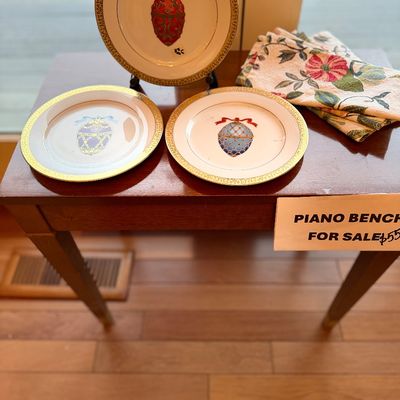 Set of three vintage Christmas ornament themed decorative porcelain plates with gold rims, displayed on a wooden bench alongside folded...