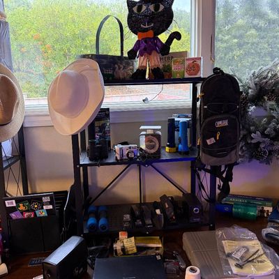 A collection of assorted household goods including Halloween decorations, sun hats, a CamelBak backpack, small electronics, and office...
