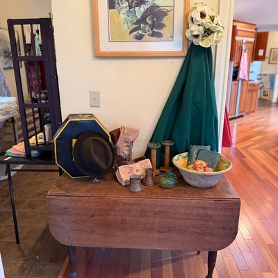 Vintage wooden drop-leaf table displaying various home decor items, including a fedora, a framed still-life print, small wooden spools,...