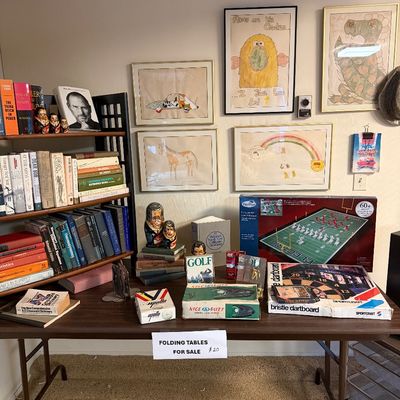 Collection of vintage items arranged on a folding table and wooden bookshelf, including board games, golf novelties, books, nesting...