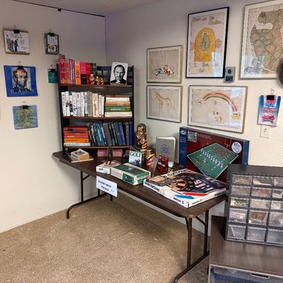 A collection of vintage books, games, framed wall art, and small storage organizers displayed on a brown folding table and surrounding...