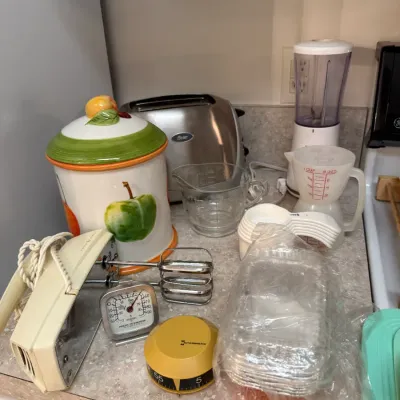 Sale Photo Thumbnail #70: Collection of kitchen items including a ceramic fruit canister, vintage hand mixer, stainless steel Oster toaster, measuring cups, and a yellow Intermatic kitchen timer.