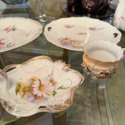Sale Photo Thumbnail #45: Collection of vintage floral porcelain tableware, including a shell-shaped dish with gilt trim, a footed teacup, and matching serving plates.