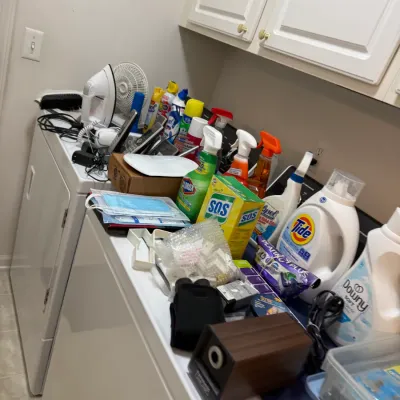 Sale Photo Thumbnail #64: Assortment of household cleaning supplies, laundry detergents, irons, and small electrics arranged on top of a washer and dryer.