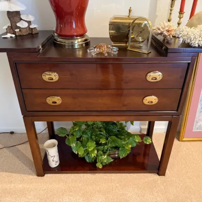 Sale Photo Thumbnail #19: Vintage campaign-style flip-top dry bar cabinet in cherry finish, featuring two drawers with recessed brass handles and an open lower shelf.