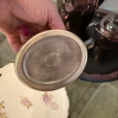 Sale Photo Thumbnail #48: Underside maker's mark on a vintage Community Achievement silverplate tea set piece, displayed with coordinating silver service pieces.