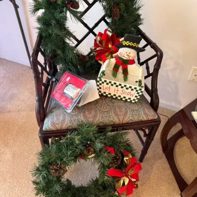 Sale Photo Thumbnail #32: Collection of holiday decorations, including faux pine wreaths with red bows, a wooden snowman container, and an indoor timer, arranged on a faux bamboo armchair.