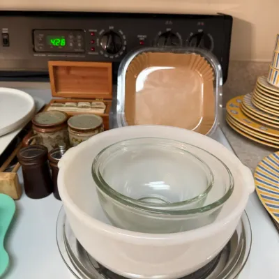 Sale Photo Thumbnail #68: Collection of kitchenware items including a white milk glass bowl nesting two clear glass mixing bowls, alongside stoneware mugs, wooden salt and pepper shakers, and stacked dishware.